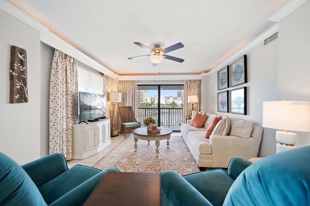 A living room features a beige sofa, two teal armchairs, and a balcony with water views — 1651 SAND KEY ESTATES COURT UNIT 28, CLEARWATER BEACH, FL
