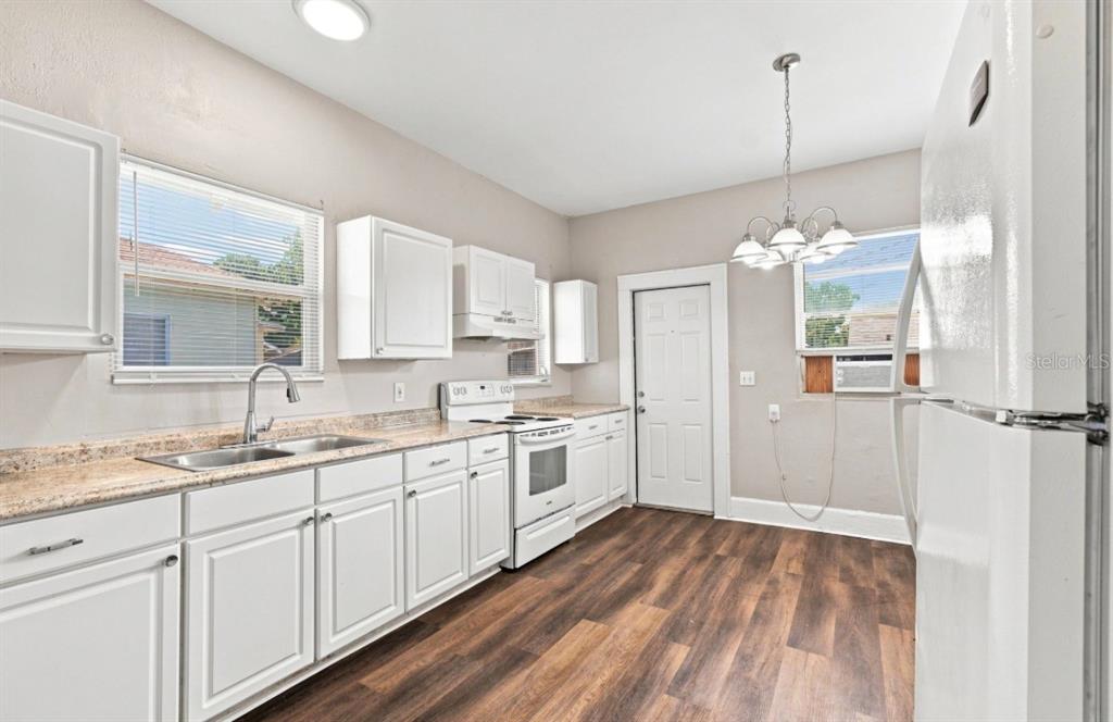A kitchen features white cabinets, a white stove, a refrigerator, and wood-look flooring — 1140 10TH AVENUE S, ST PETERSBURG, FL