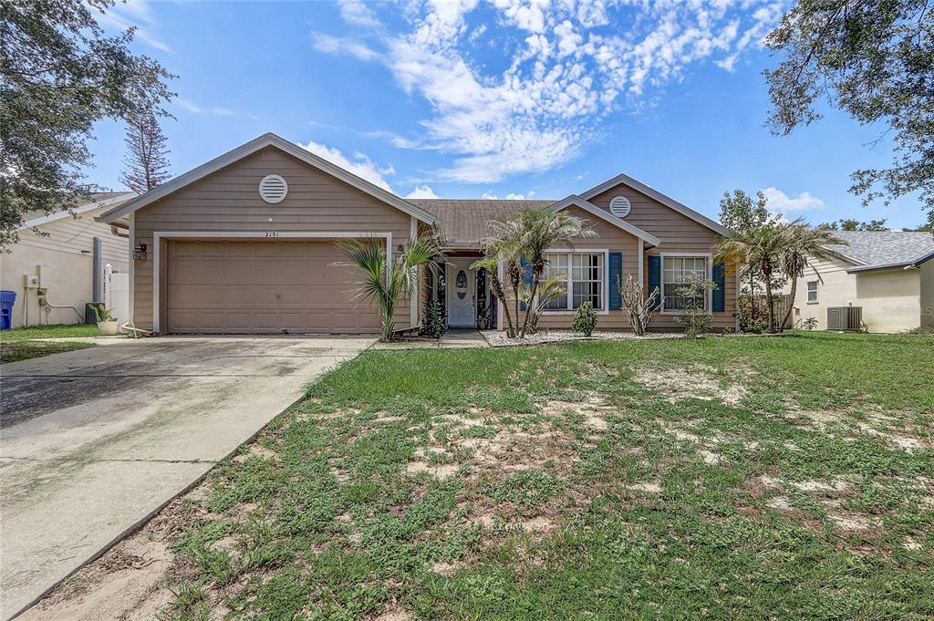 A single-story suburban house with beige siding, a two-car garage, and a front lawn — 2191 ALCLOBE CIRCLE, OCOEE, FL