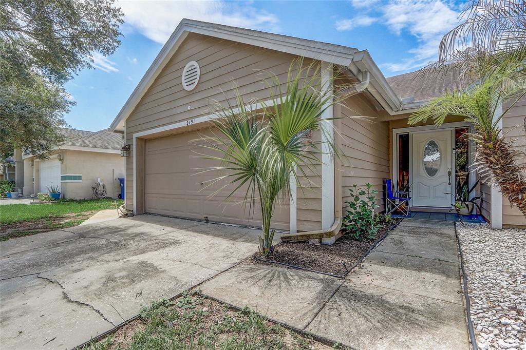 A tan house exterior features a two-car garage, a front walkway, and a small palm tree — 2191 ALCLOBE CIRCLE, OCOEE, FL