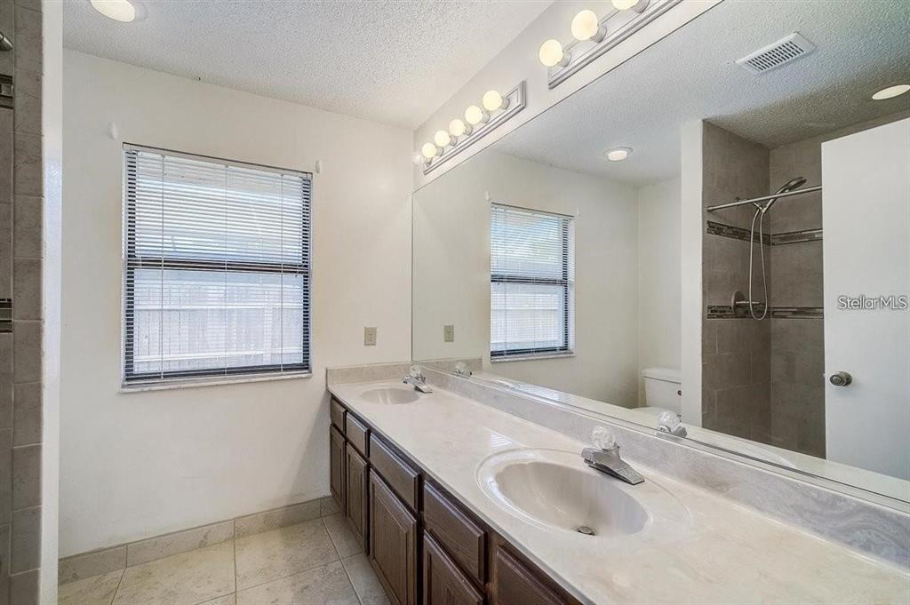 A bathroom features a double vanity with dark wood cabinets, a large mirror, and shower — 6483 JARVIS ROAD, SARASOTA, FL