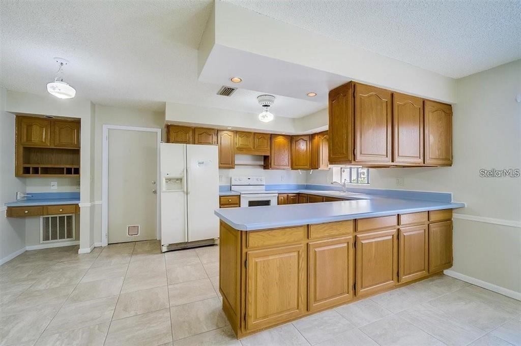 A kitchen features wood cabinets, blue laminate countertops, white appliances, and light-colored tile flooring — 6483 JARVIS ROAD, SARASOTA, FL