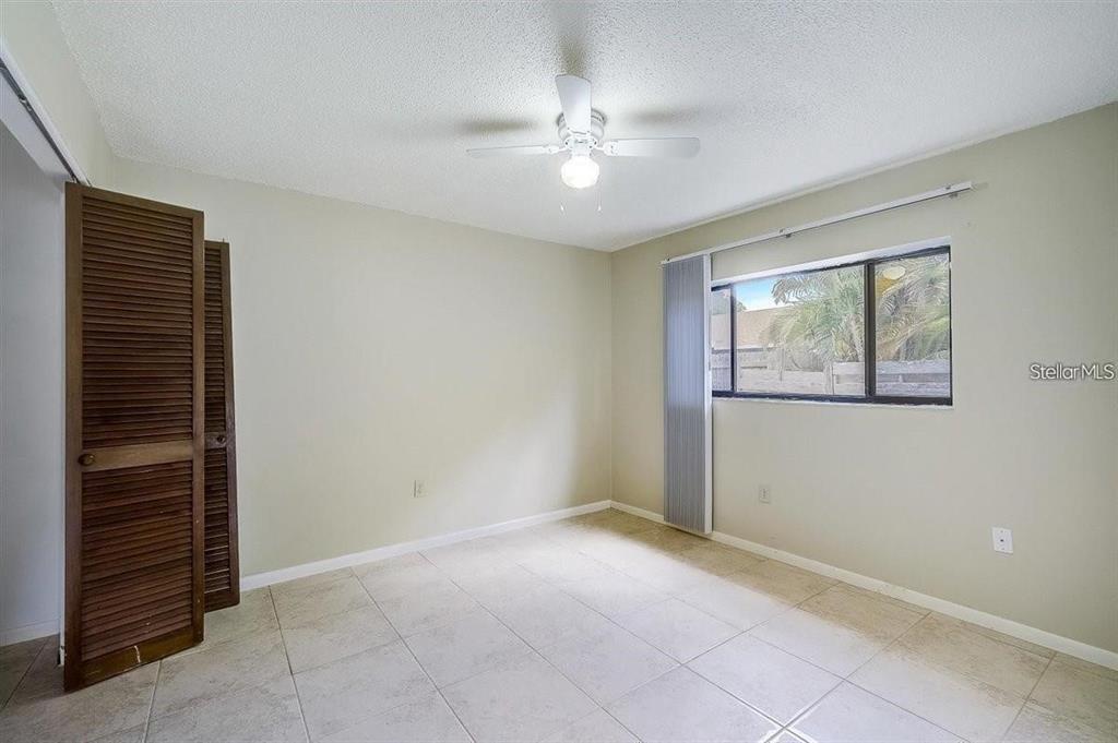 An empty bedroom features light-colored walls, tile flooring, a ceiling fan, and louvered closet doors — 6483 JARVIS ROAD, SARASOTA, FL
