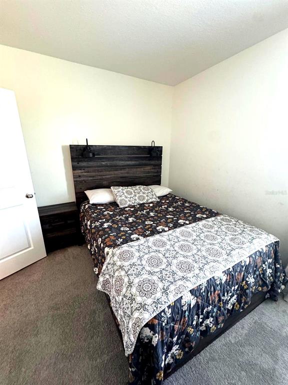 A bedroom features a dark wood plank headboard, a floral patterned quilt, and gray carpeting — 10570 PENNY GALE LOOP, SAN ANTONIO, FL