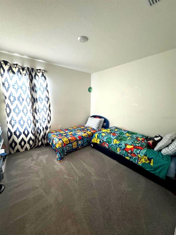 A bedroom features two twin beds with patterned bedding and floor-length curtains — 10570 PENNY GALE LOOP, SAN ANTONIO, FL