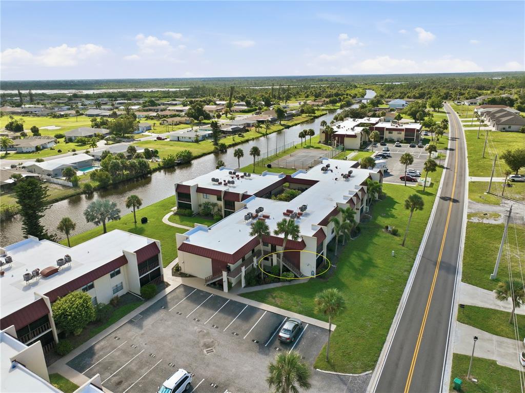 An aerial view shows multi-story apartment buildings with red roofs near a canal and road — 72 BOUNDARY BOULEVARD UNIT 210, ROTONDA WEST, FL