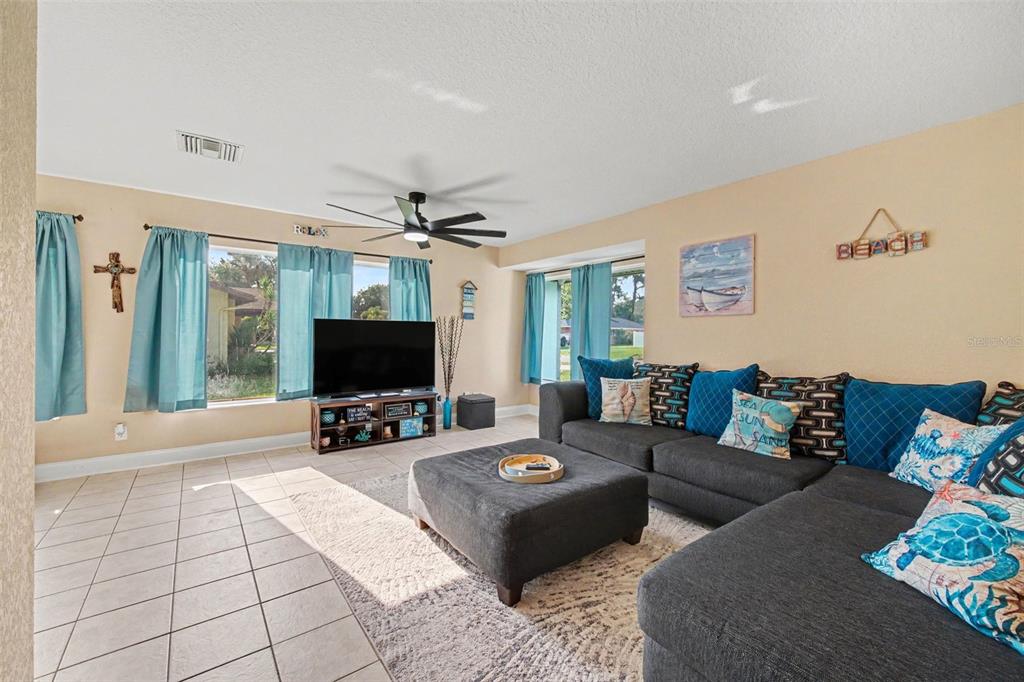 A living room features a dark sectional sofa, a large ottoman, and light-colored tile flooring — 3 CLARK LANE, PALM COAST, FL