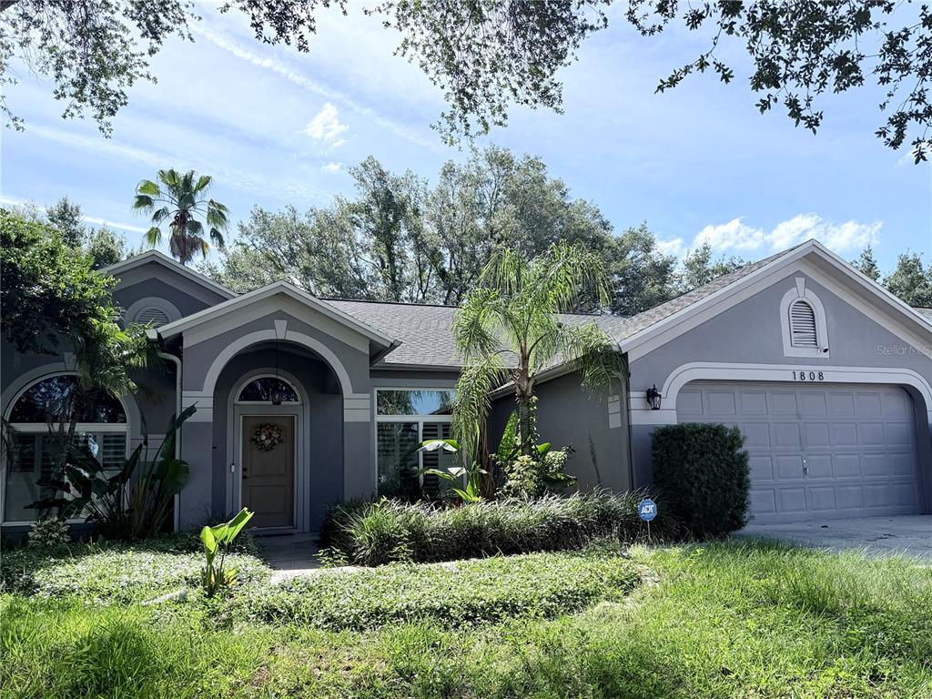A single-story gray house with a two-car garage, arched entryway, and mature landscaping — 1808 POWDER RIDGE DRIVE, VALRICO, FL
