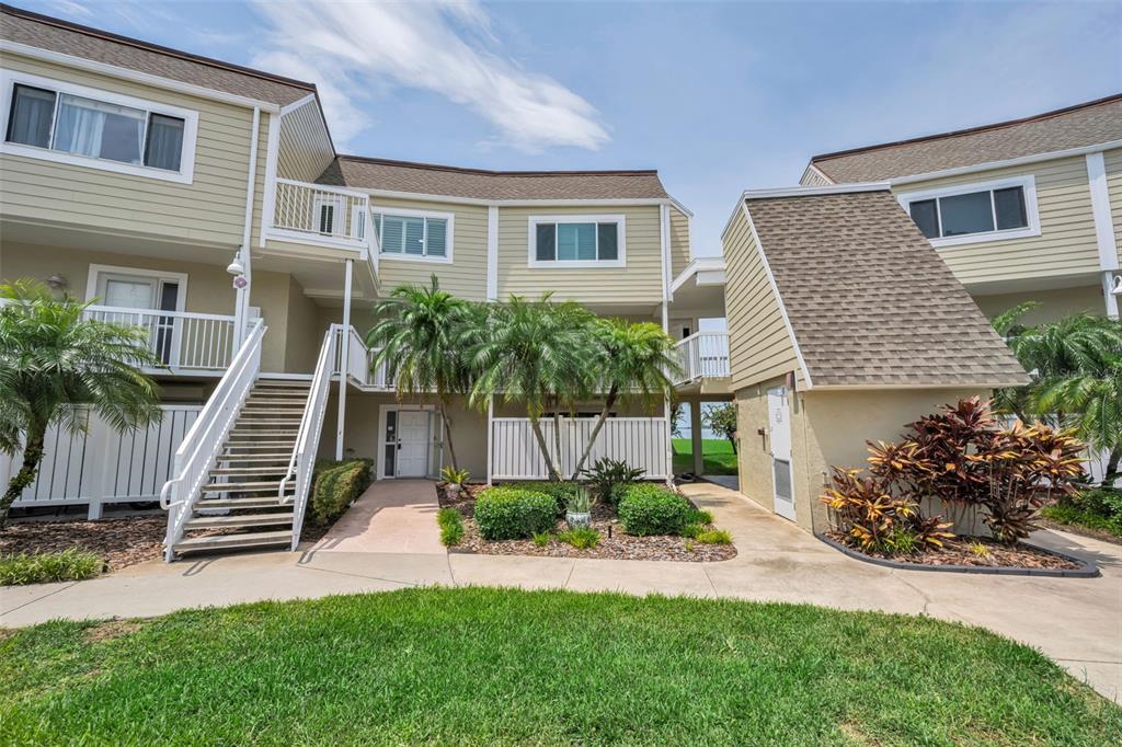 A two-story tan building with a staircase, palm trees, and a concrete walkway — 433 S PAULA DRIVE UNIT 32, DUNEDIN, FL