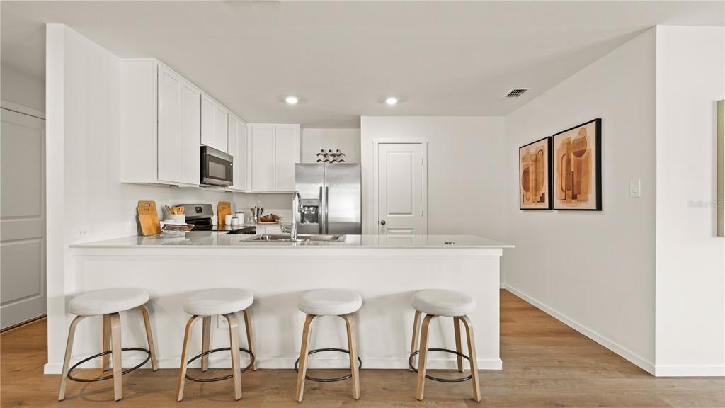 A modern kitchen features white cabinets, stainless steel appliances, a breakfast bar, and four stools — 331 NOLA LANE, DUNDEE, FL