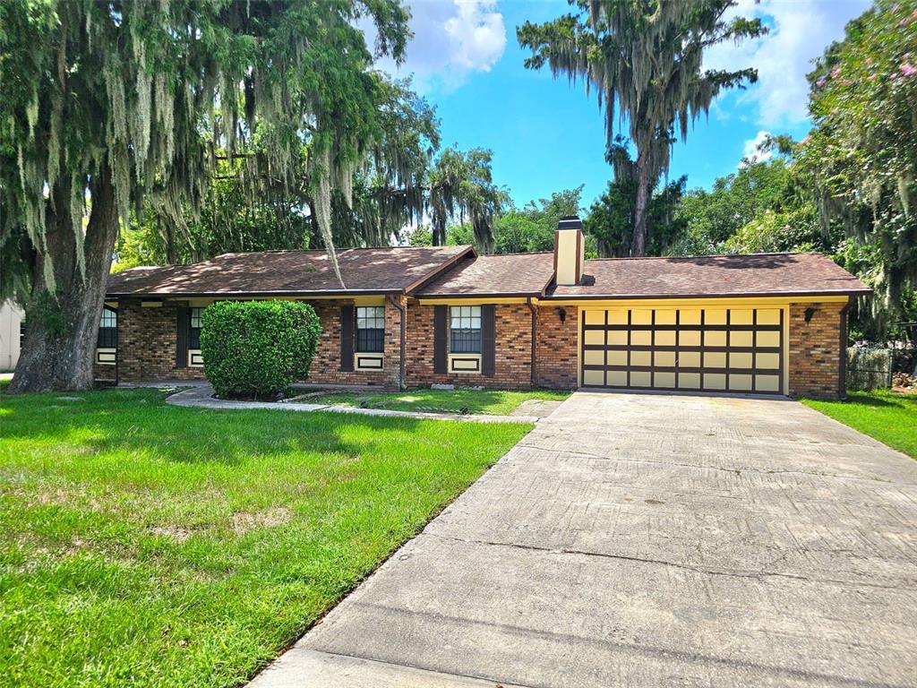A single-story brick house with a two-car garage, brown roof, and large mossy trees — 1292 E LAKE SHORE BOULEVARD, KISSIMMEE, FL