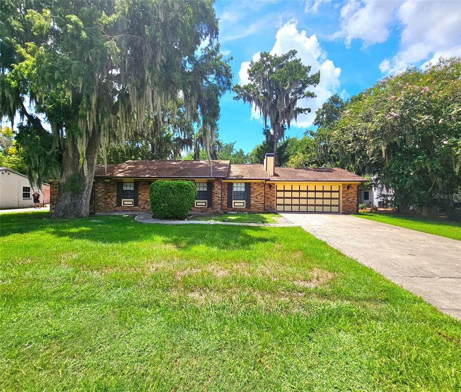 A single-story brick house with a two-car garage and large trees in the front yard — 1292 E LAKE SHORE BOULEVARD, KISSIMMEE, FL