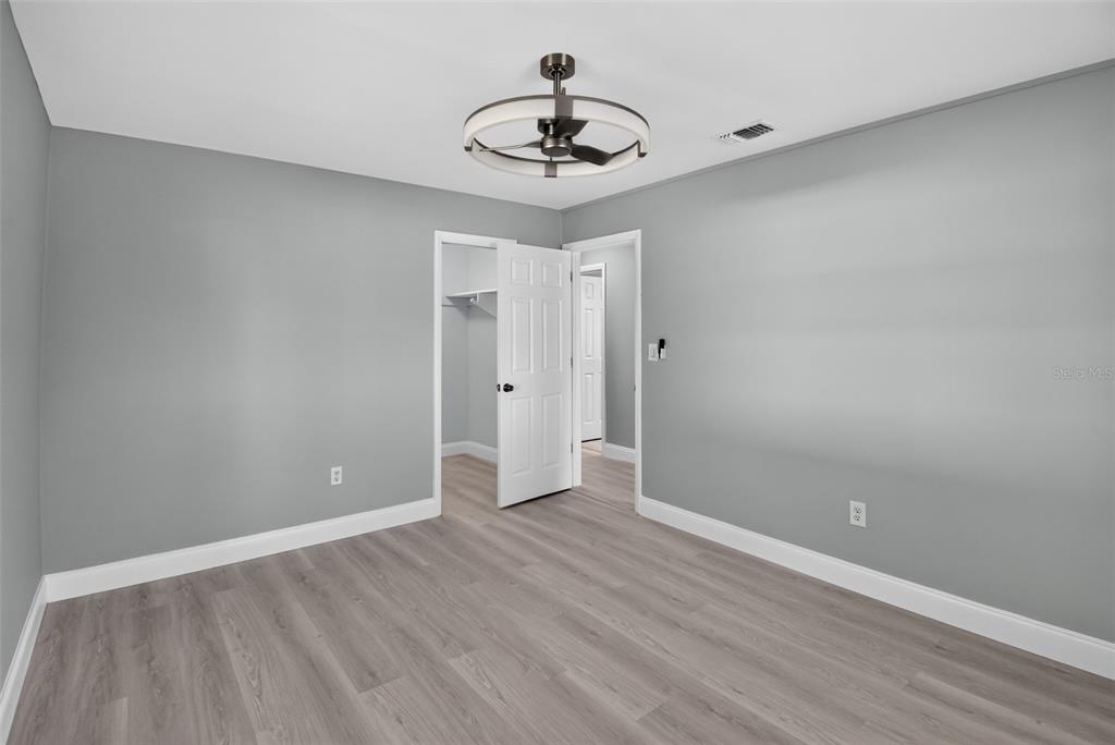 A bedroom with sage green walls, light wood-look flooring, a ceiling fan, and white closet doors — 1148 FOUNTAINHEAD DRIVE, DELTONA, FL