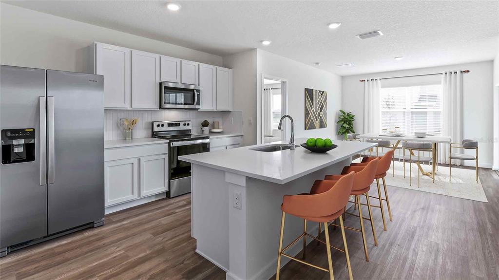 A modern kitchen features white cabinetry, stainless steel appliances, a central island, and bar stools — 11975 FALLOW DOWN DRIVE, DADE CITY, FL