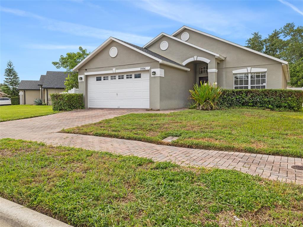 A single-story house with a beige stucco exterior, a two-car garage, and a paved driveway — 9996 PORTOFINO DRIVE, ORLANDO, FL