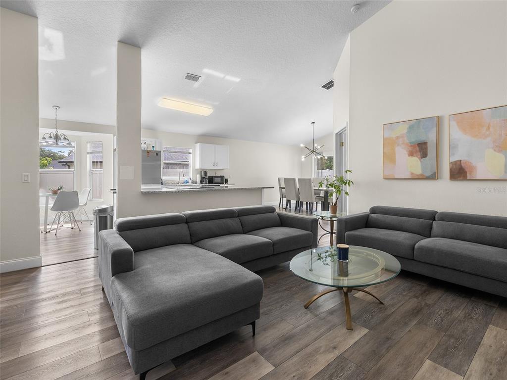 A living room with gray sectionals and a glass coffee table opens to a kitchen — 9996 PORTOFINO DRIVE, ORLANDO, FL