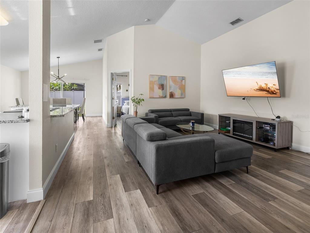A living room with gray sectional seating, a wall-mounted television, and wood-look flooring — 9996 PORTOFINO DRIVE, ORLANDO, FL