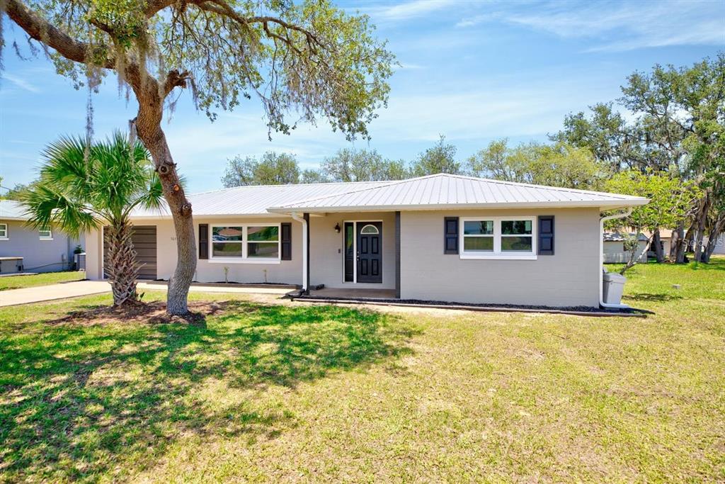 A single-story house with a light-colored exterior, a metal roof, and a dark front door — 503 RICH STREET, AVON PARK, FL
