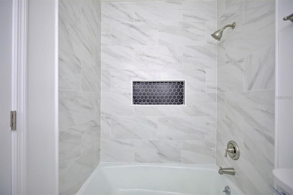 A bathtub shower combination features white marble-look wall tiles and a dark hexagonal tile niche — 503 RICH STREET, AVON PARK, FL