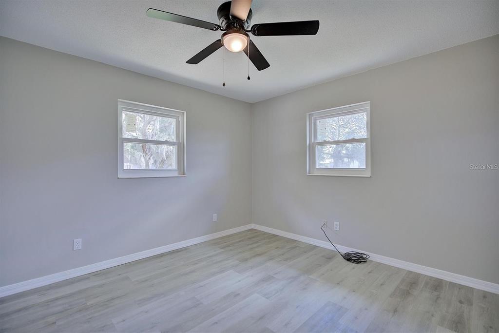 A bedroom with light gray walls, wood-look flooring, two windows, and a ceiling fan — 503 RICH STREET, AVON PARK, FL