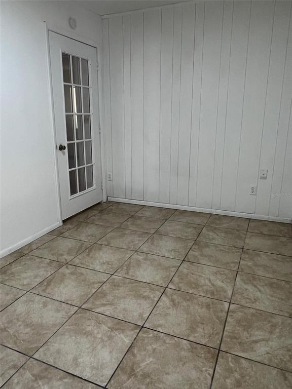 An empty room features white wood-paneled walls, a glass-paned door, and light-colored tile flooring — 29 MIAMI DRIVE, LAKE PLACID, FL