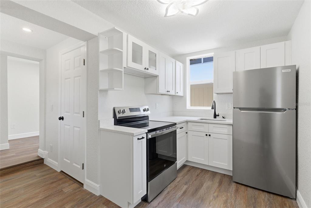 A kitchen features white cabinets, stainless steel appliances, and wood-look flooring — 113 145TH AVENUE E UNIT 6, MADEIRA BEACH, FL