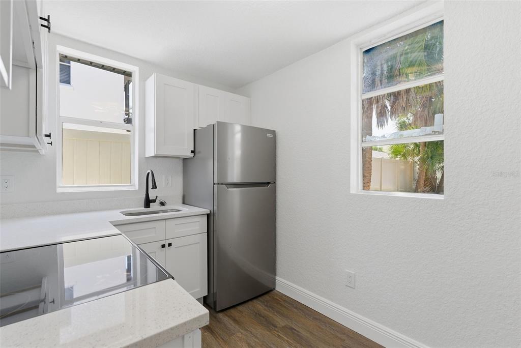 A kitchen features white cabinets, a stainless steel refrigerator, a sink, and two windows — 113 145TH AVENUE E UNIT 6, MADEIRA BEACH, FL