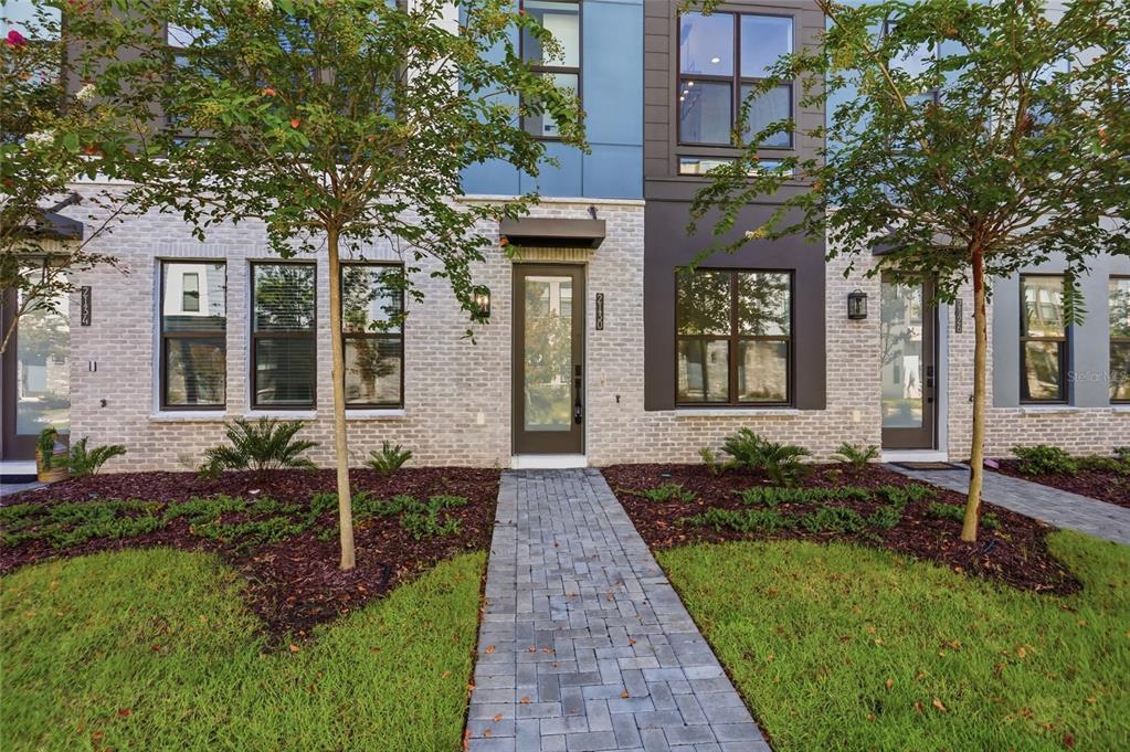A modern townhome exterior features white brick, blue paneling, and a paved walkway — 2130 WHITNEY MARSH ALLEY, ORLANDO, FL