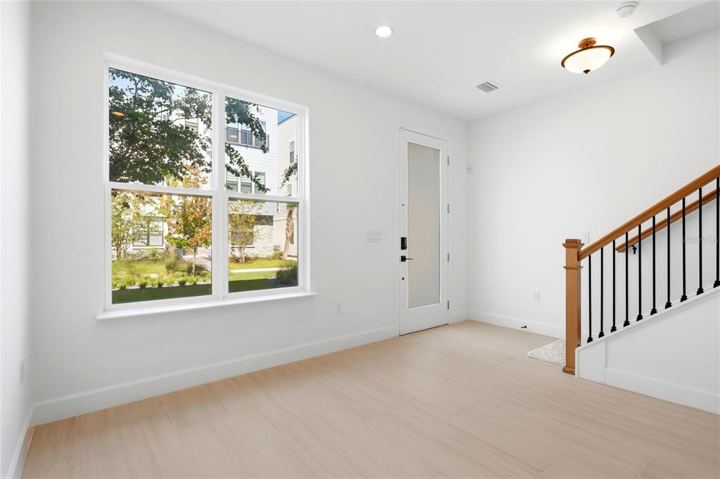 A bright room features light wood-look flooring, a large window, a glass-paneled door, and stairs — 2130 WHITNEY MARSH ALLEY, ORLANDO, FL