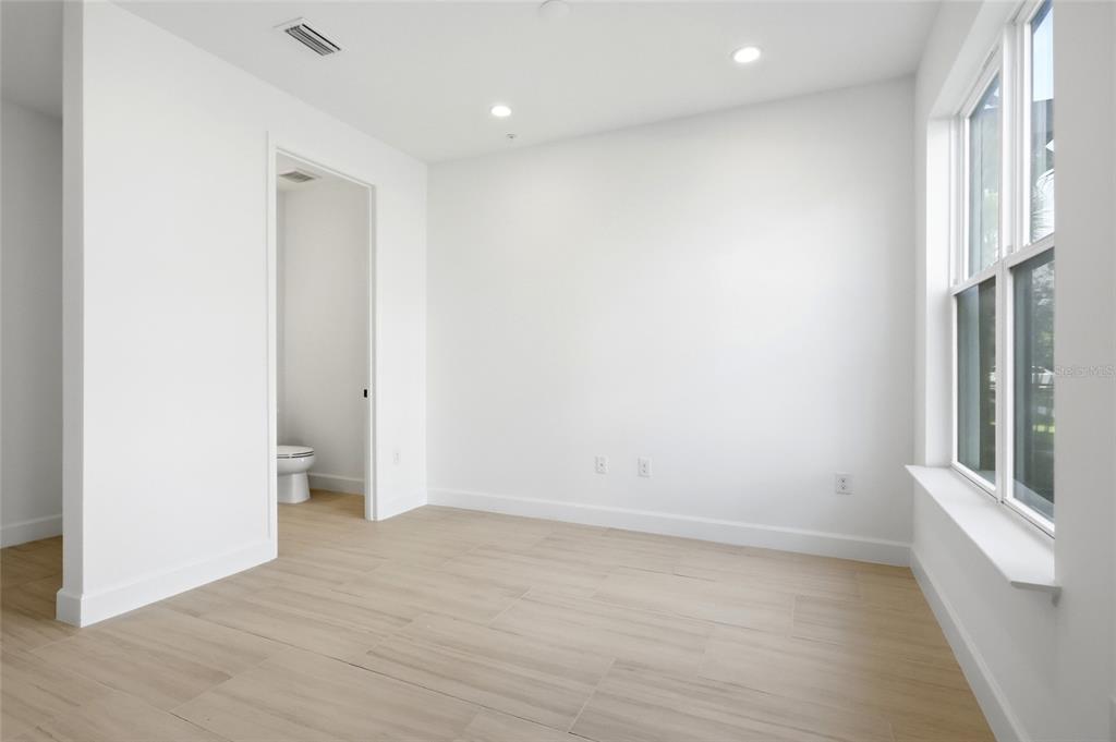 A bright, empty room features white walls, light wood-look tile flooring, recessed lighting, and a bathroom — 2130 WHITNEY MARSH ALLEY, ORLANDO, FL