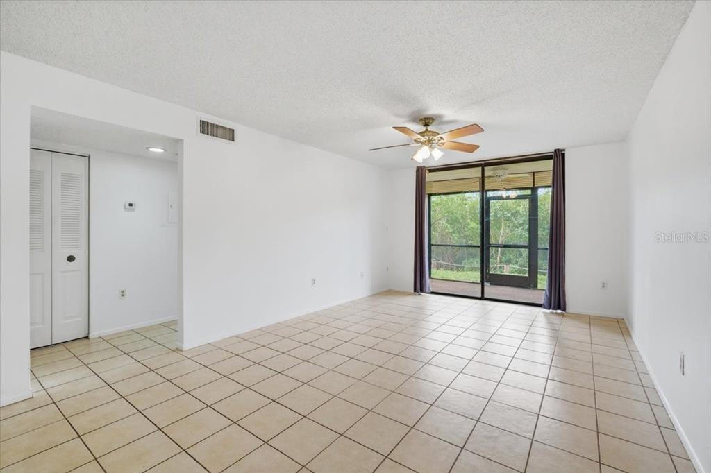 An empty living room features white walls, beige tile flooring, and a sliding glass door — 1332 PASADENA AVENUE S UNIT 102, SOUTH PASADENA, FL