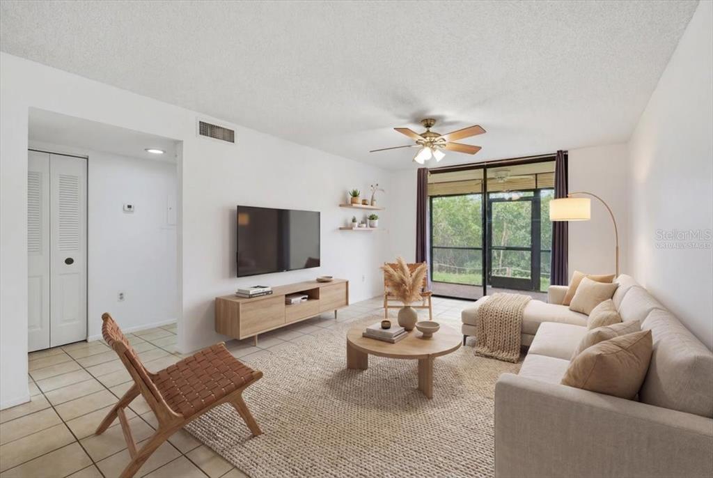 A living room with white walls, tile flooring, a ceiling fan, and a sliding glass door — 1332 PASADENA AVENUE S UNIT 102, SOUTH PASADENA, FL
