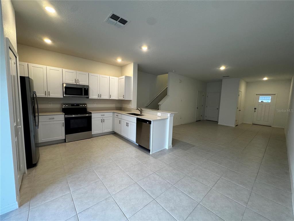 A kitchen with white cabinets, stainless steel appliances, and tile flooring opens to a living area — 10149 TRUMPET HONEYSUCKLE WAY, SAN ANTONIO, FL