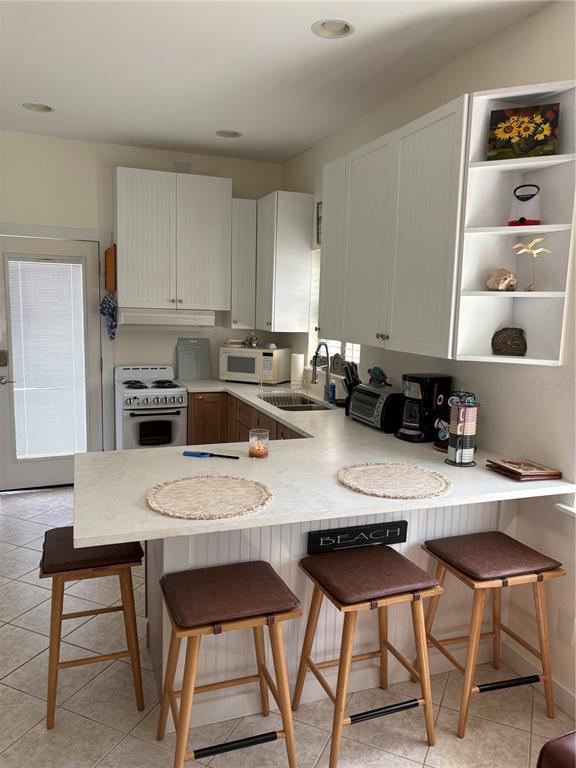A kitchen features white cabinets, a breakfast bar with four stools, and a gas stove — 101 E BAY DRIVE, TREASURE ISLAND, FL
