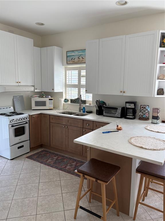 A kitchen features white upper cabinets, wood lower cabinets, a white stove, and a breakfast bar — 101 E BAY DRIVE, TREASURE ISLAND, FL