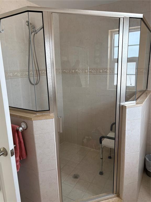 A tiled walk-in shower features a glass enclosure, a handheld showerhead, and a shower chair — 101 E BAY DRIVE, TREASURE ISLAND, FL