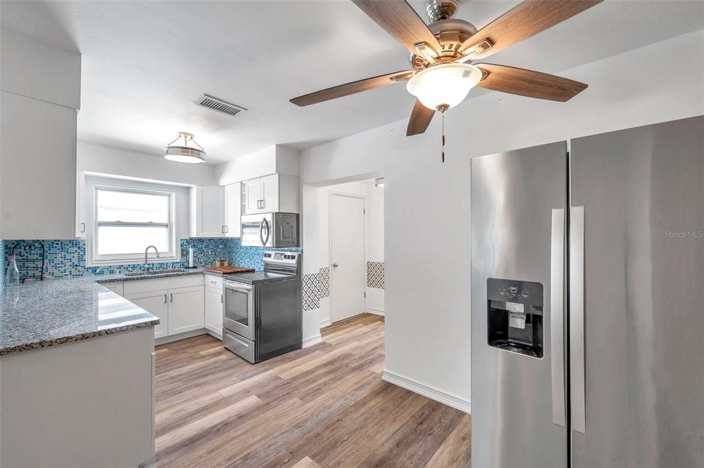 A kitchen features white cabinets, granite countertops, stainless steel appliances, and wood-look flooring — 5900 CYPRESS STREET N, ST PETERSBURG, FL