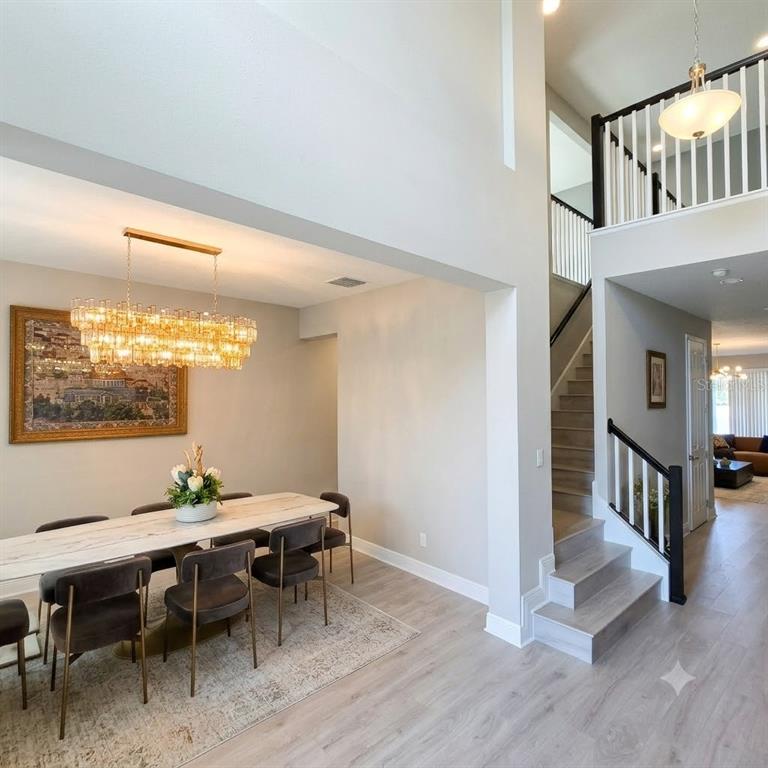 A dining area with a crystal chandelier and a staircase with black railings — 1952 DRUMMOND POINT, WESLEY CHAPEL, FL