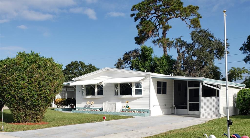 A white single-story manufactured home features a screened-in porch, a concrete driveway, and mature landscaping — 183 PHILADELPHIA BOULEVARD UNIT 22, PALM HARBOR, FL