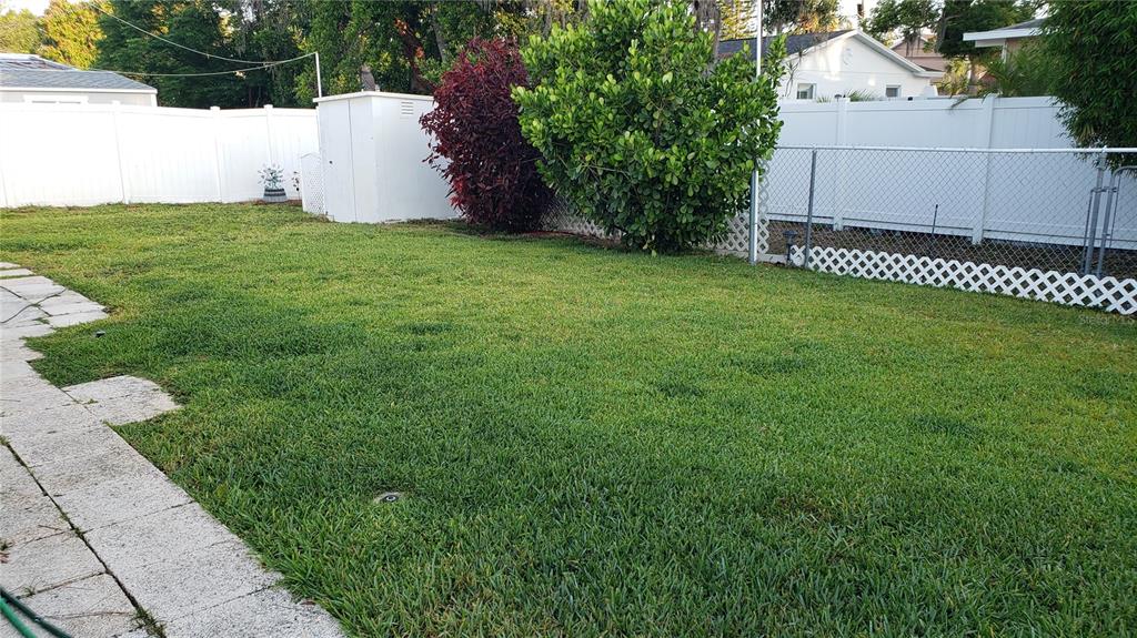 A grassy backyard features a white vinyl fence, a storage shed, and a stone walkway — 183 PHILADELPHIA BOULEVARD UNIT 22, PALM HARBOR, FL