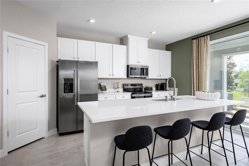 A modern kitchen features white cabinetry, stainless steel appliances, a quartz island, and bar seating — 3954 ADDIE WAY, MELBOURNE, FL