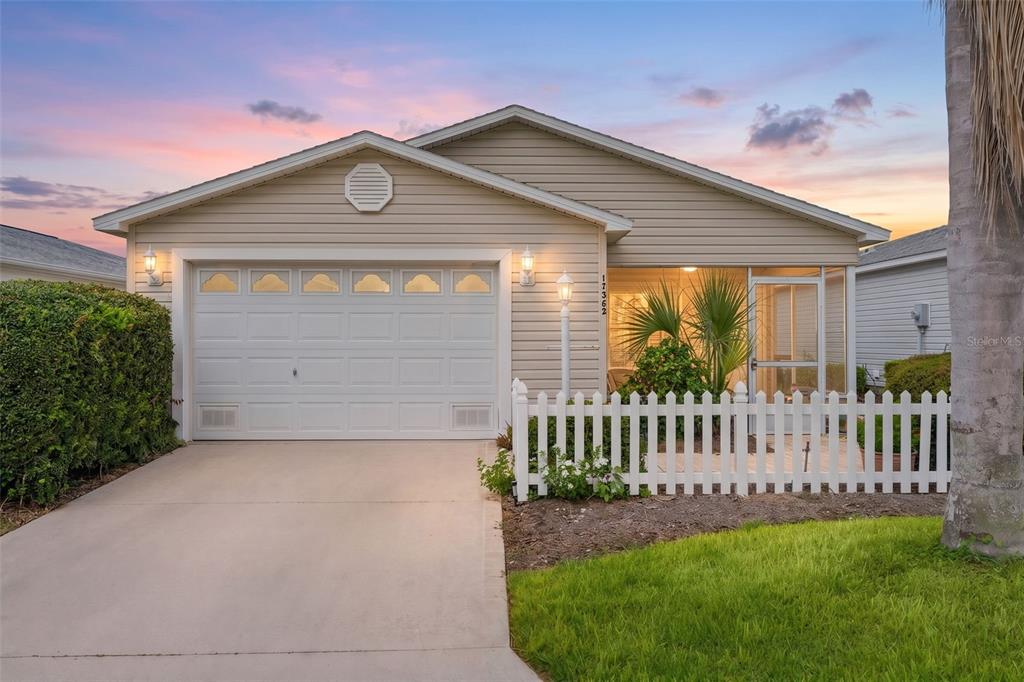 A single-story house with beige siding, a white garage door, and a screened-in front porch — 17362 SE 78TH HARMONY CIRCLE, THE VILLAGES, FL