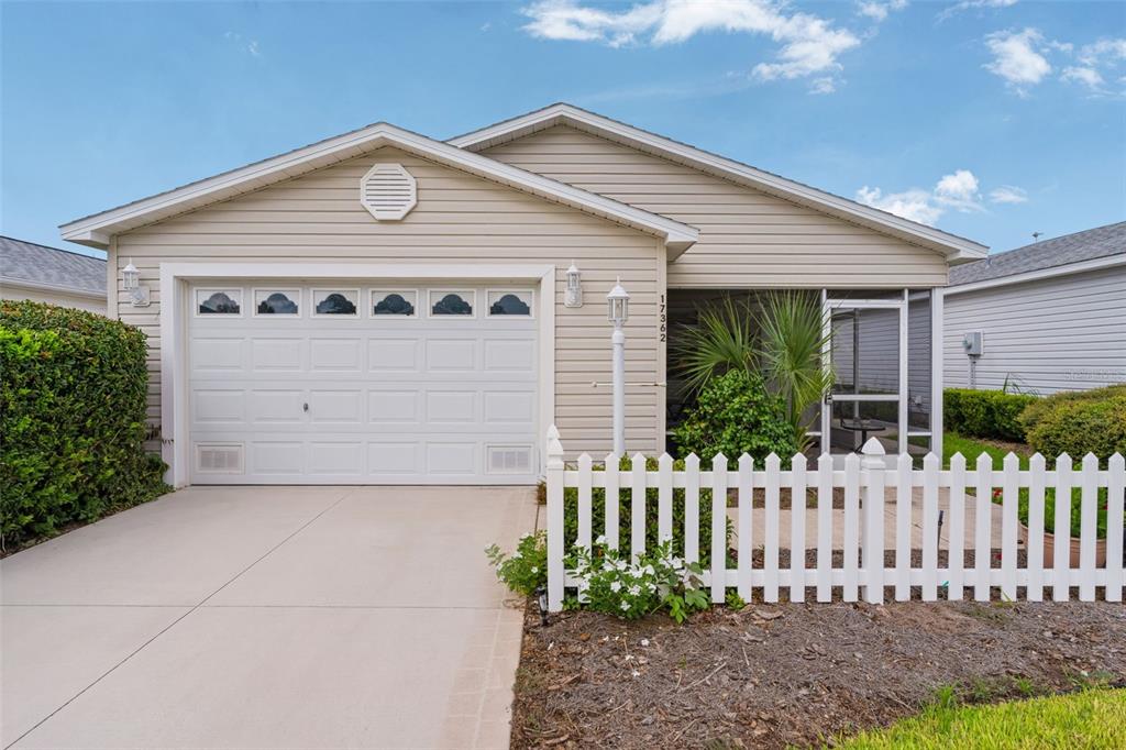 A single-story house with beige siding, a white garage door, and a front picket fence — 17362 SE 78TH HARMONY CIRCLE, THE VILLAGES, FL