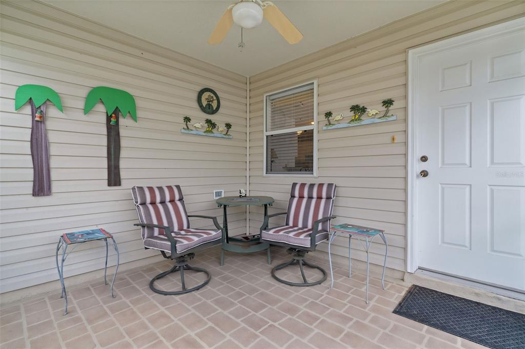 A covered porch features beige siding, two striped chairs, a small table, and palm tree decorations — 17362 SE 78TH HARMONY CIRCLE, THE VILLAGES, FL