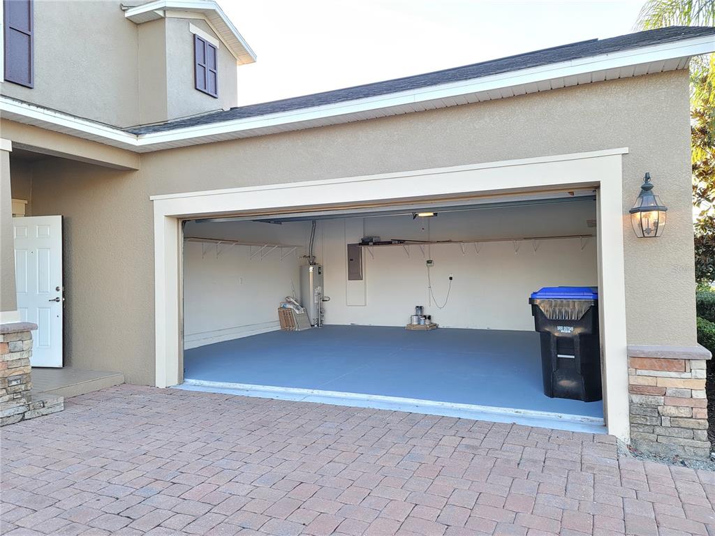 An open garage with a painted gray floor, a water heater, and a trash bin — 15030 EVERGREEN OAK LOOP, WINTER GARDEN, FL