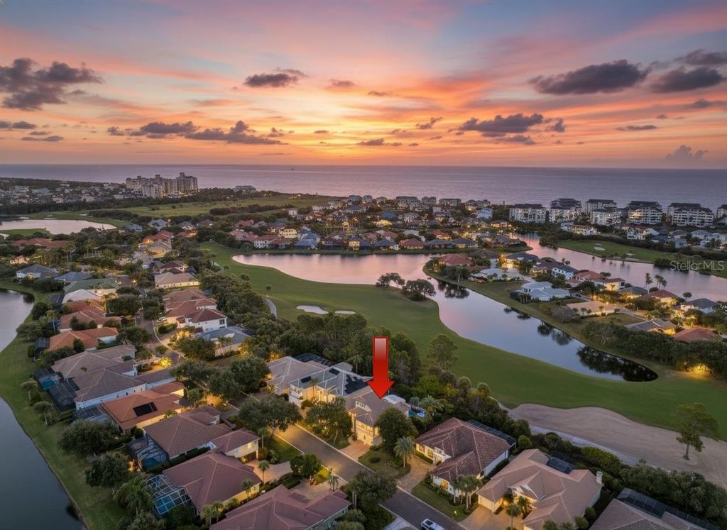 An aerial view shows a residential neighborhood with a golf course, lake, and ocean sunset — 29 OAK VIEW CIRCLE E, PALM COAST, FL