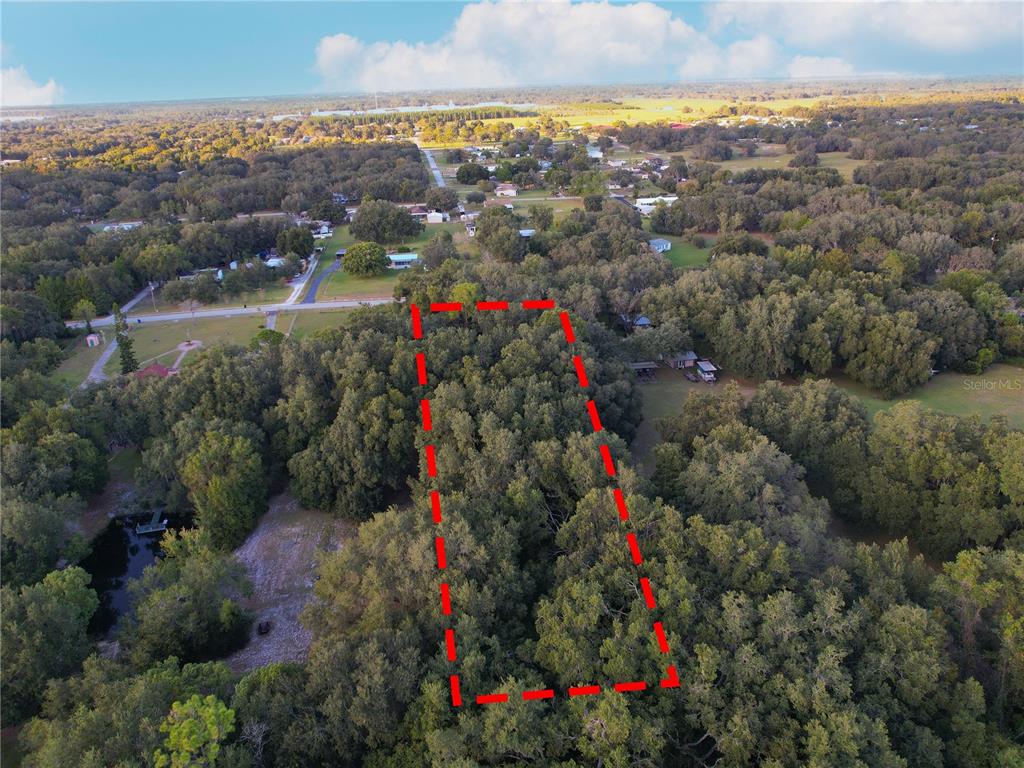 An aerial view shows a rectangular plot of land outlined in red amidst wooded surroundings — TENNESSEE AVENUE, ASTATULA, FL