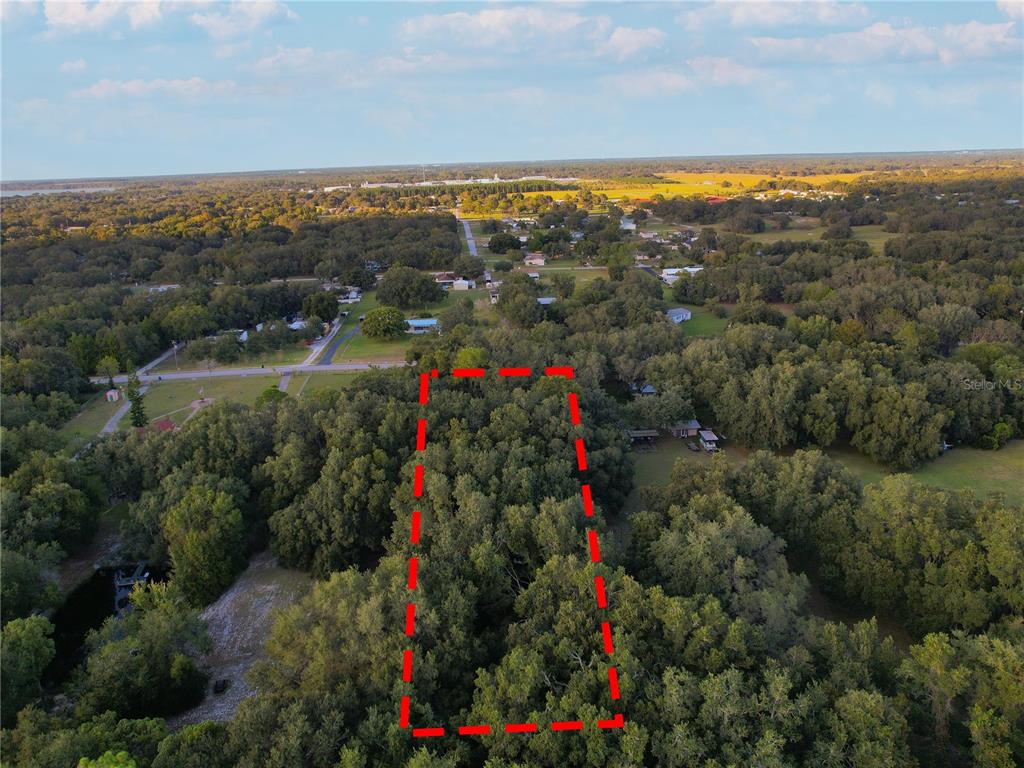 An aerial view shows a rectangular, tree-covered plot of land outlined in red — TENNESSEE AVENUE, ASTATULA, FL