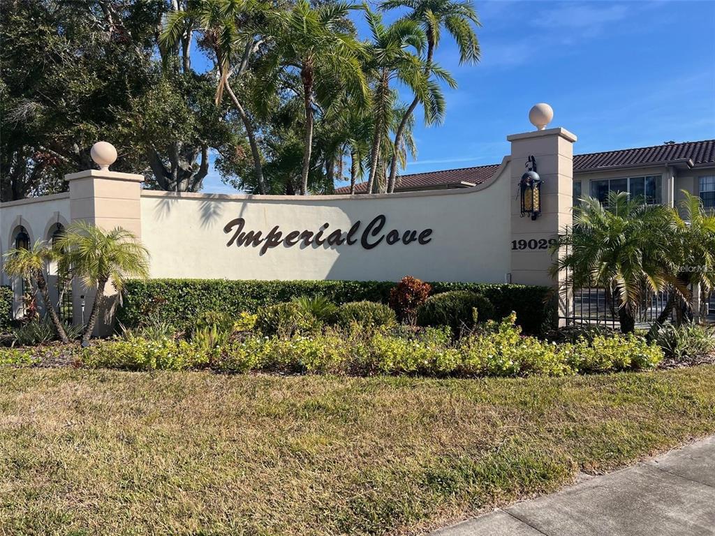 A beige stucco entrance sign for Imperial Cove stands in front of palm trees and landscaping — 19029 US HIGHWAY 19 N UNIT 6-14, CLEARWATER, FL