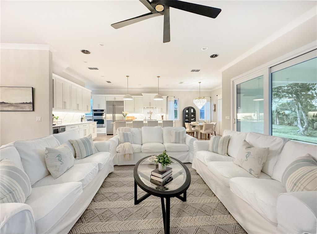 A bright, open-concept living room features white slipcovered sofas, a glass coffee table, and kitchen — 2549 PALM AVENUE, FLAGLER BEACH, FL